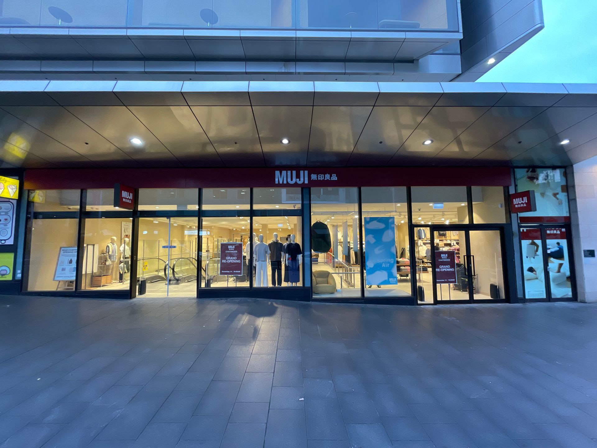 MUJI store front with glass windows, under a modern building's overhang.
