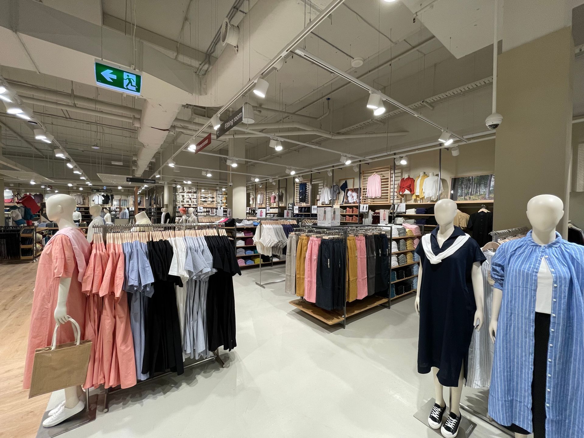 Clothing store interior with mannequins displaying summer apparel; racks of clothes and overhead lighting.