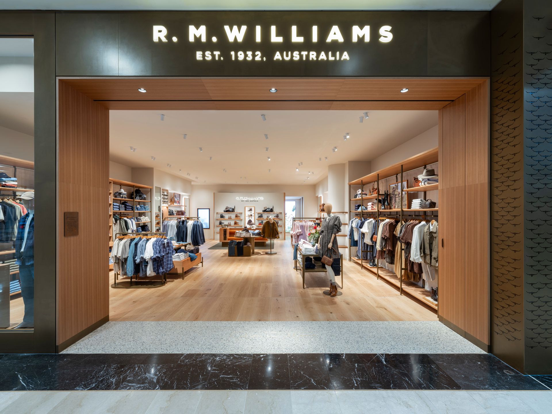 Exterior of an R.M. Williams store with a wooden frame entrance.  Clothing displayed inside, with the brand name above the door.