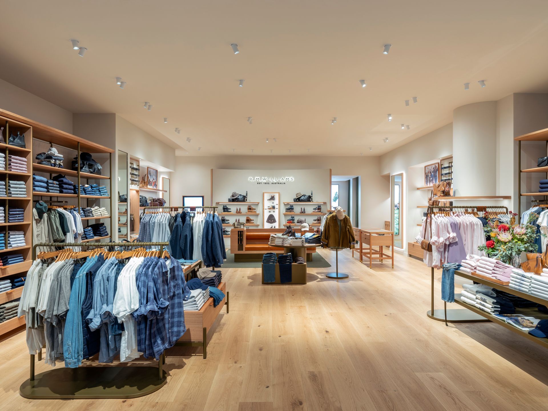 Clothing store interior: wooden floors, clothing racks, denim displayed, neutral color palette, well-lit.