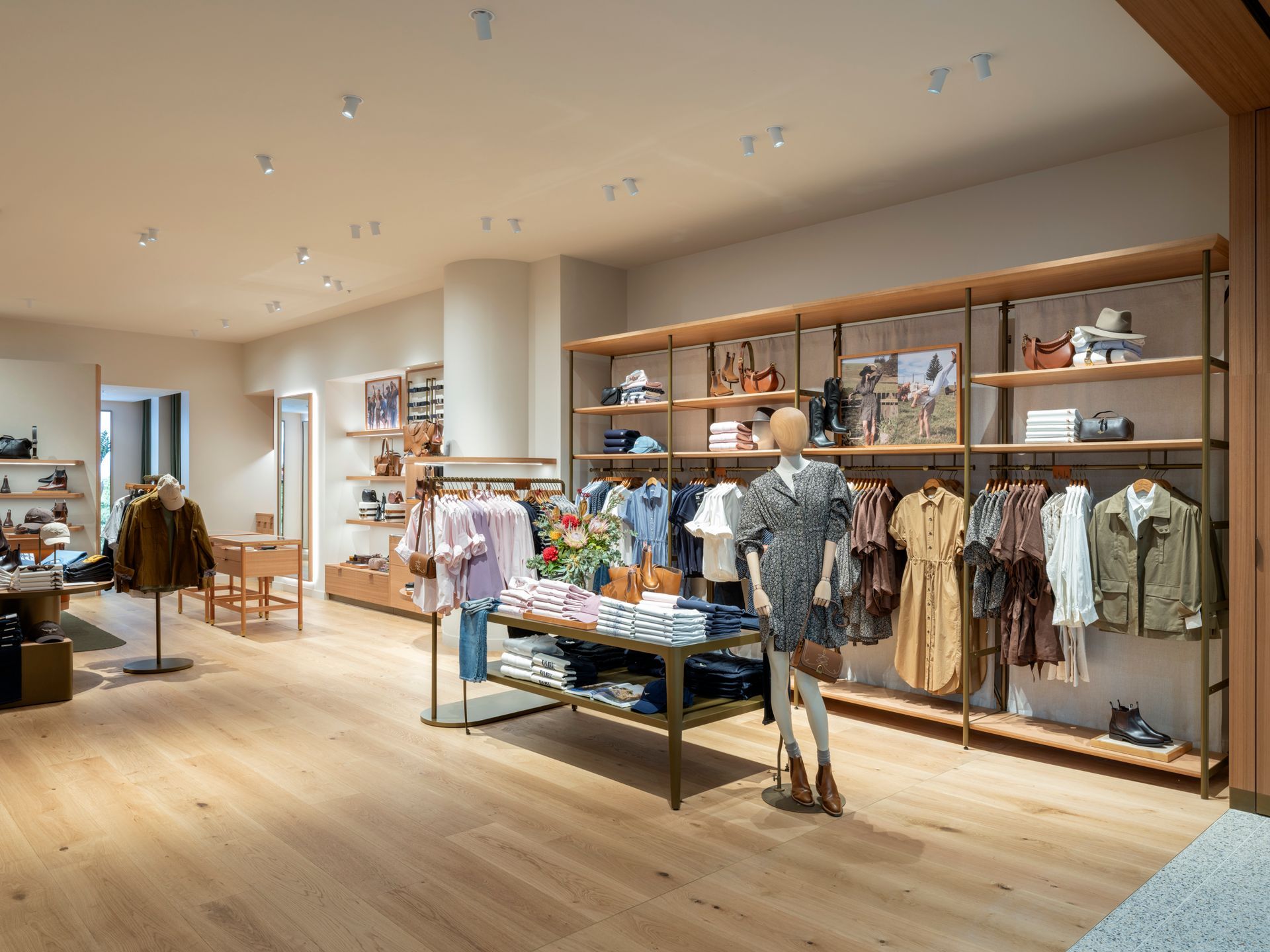 Clothing store interior with wooden floors, light walls, and merchandise displays.