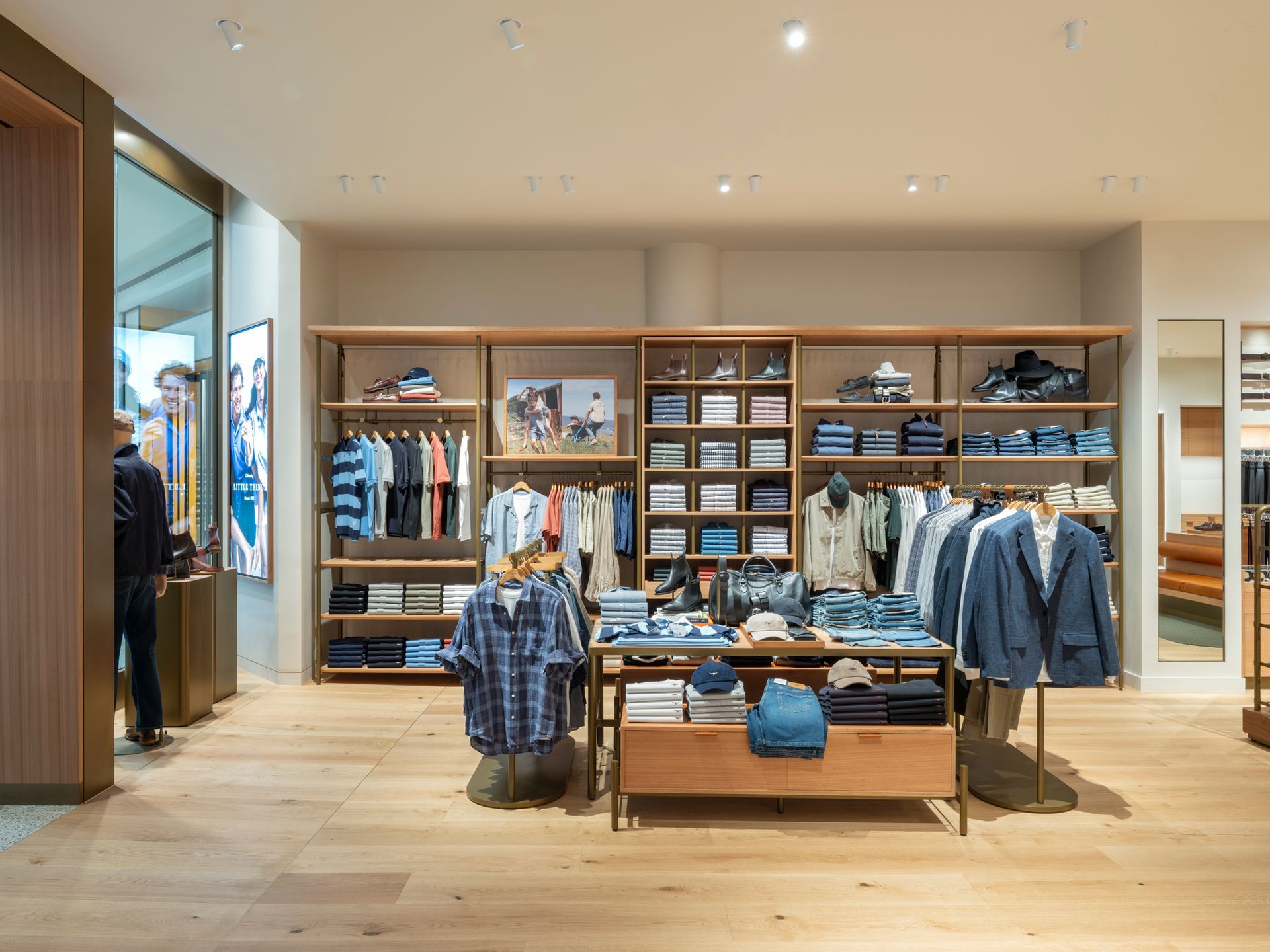 Clothing store interior with wooden shelving displaying folded and hanging apparel.