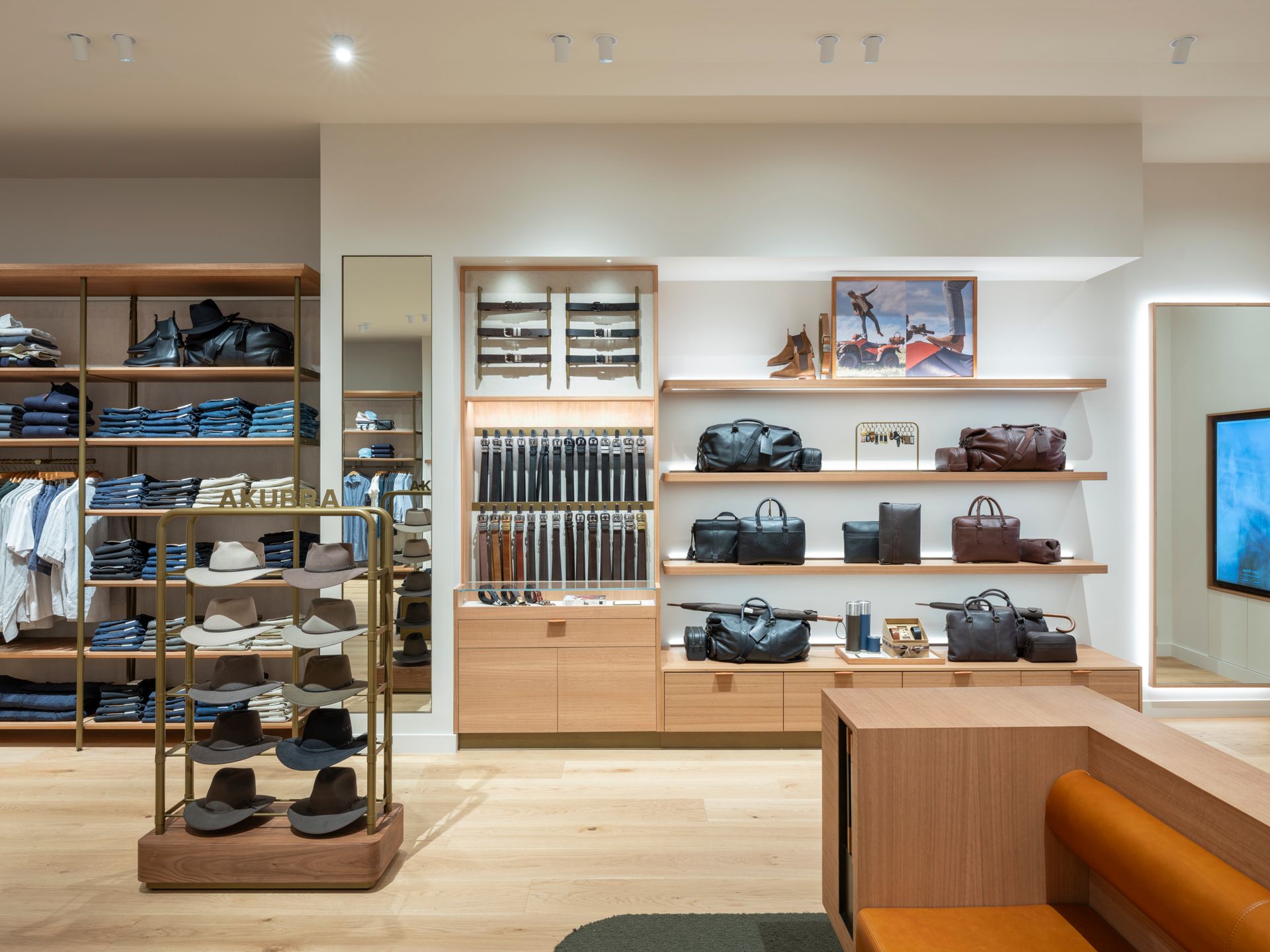 Interior view of a clothing store with wood shelves displaying denim, hats, belts, bags, and shoes.