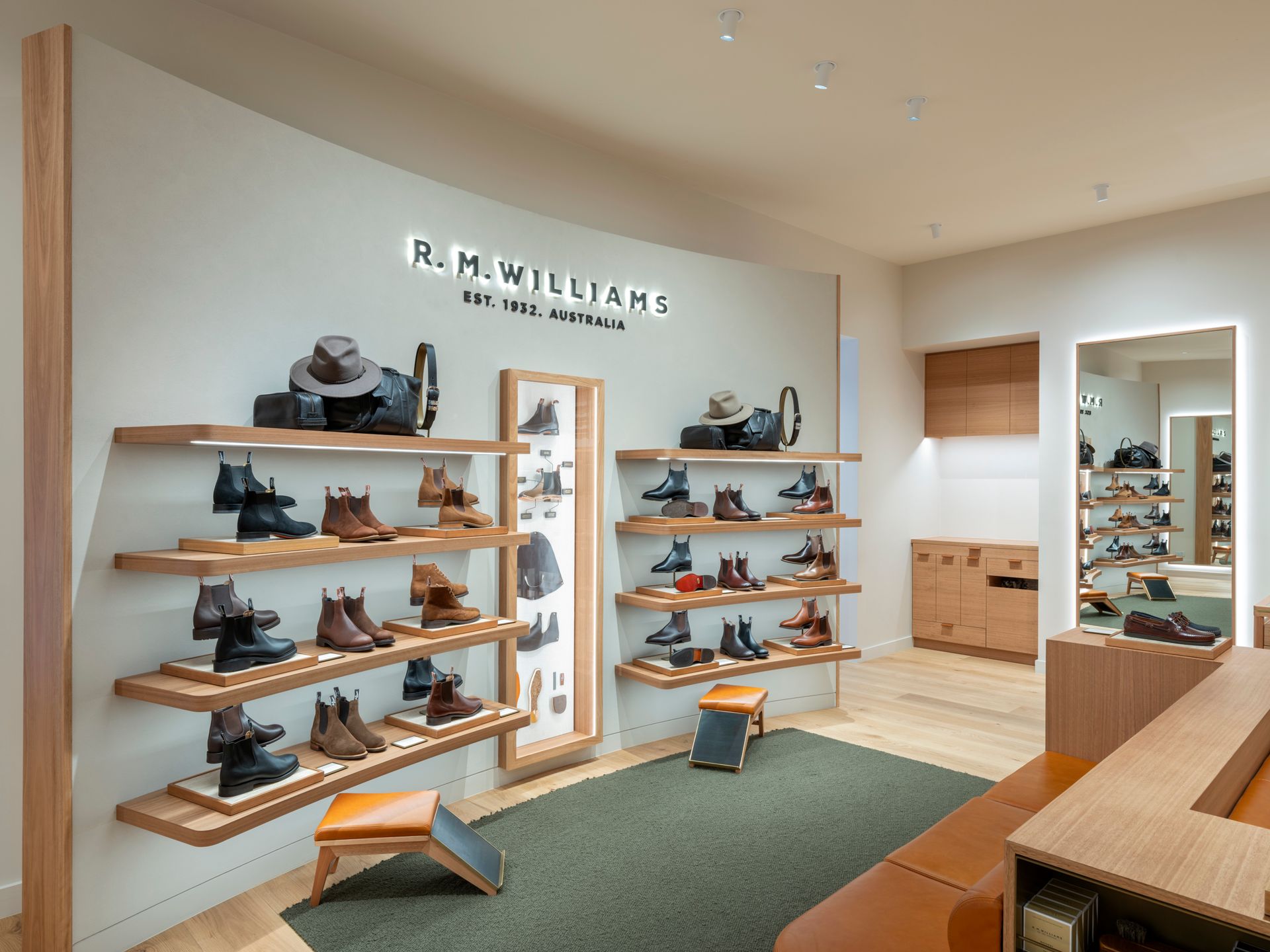 Interior of an R.M. Williams store, displaying boots and accessories on wooden shelves against a light gray wall.