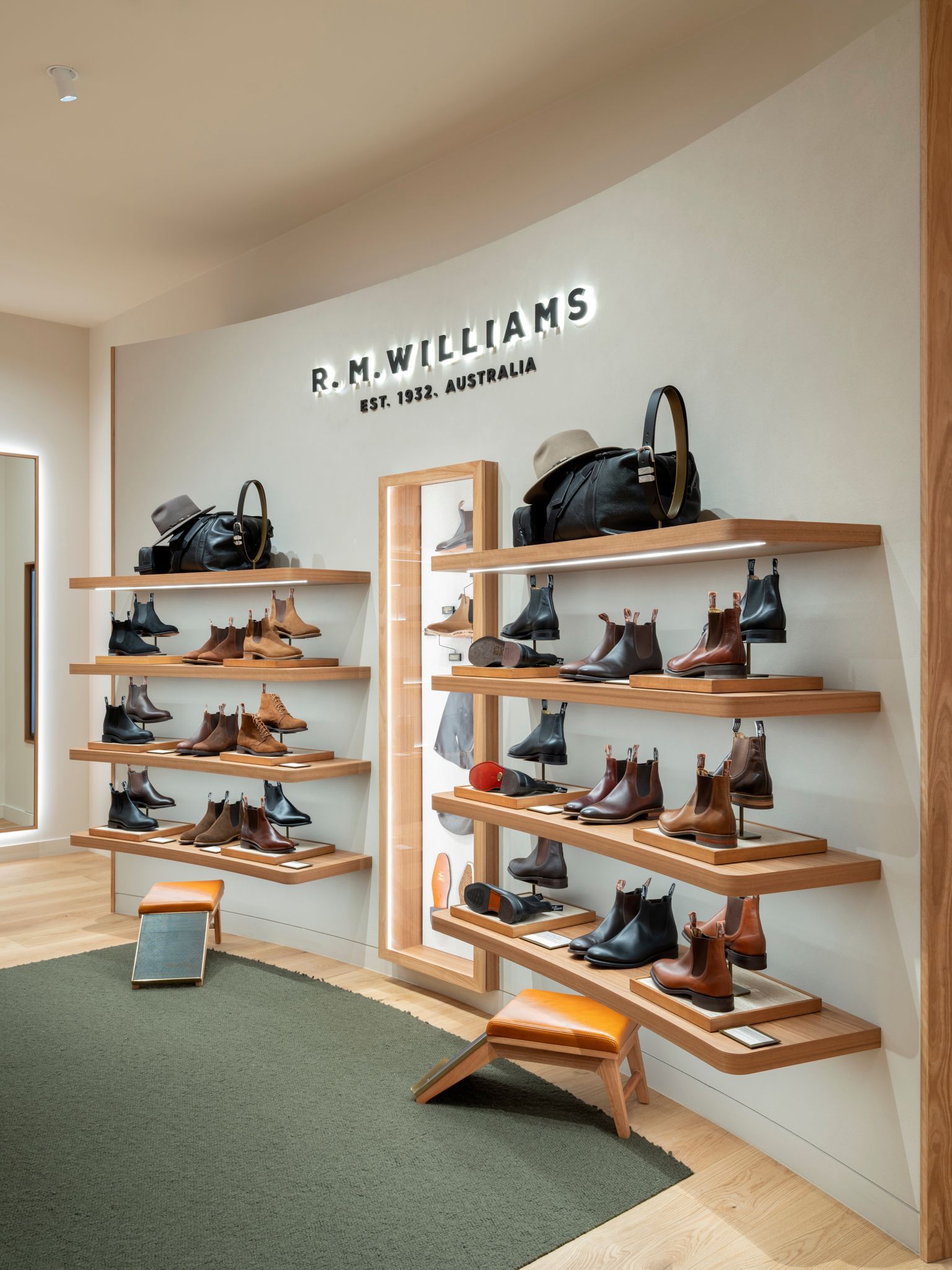 Interior of a P.M. Williams store with shelves displaying boots and accessories. Neutral tones with wooden accents and green carpet.