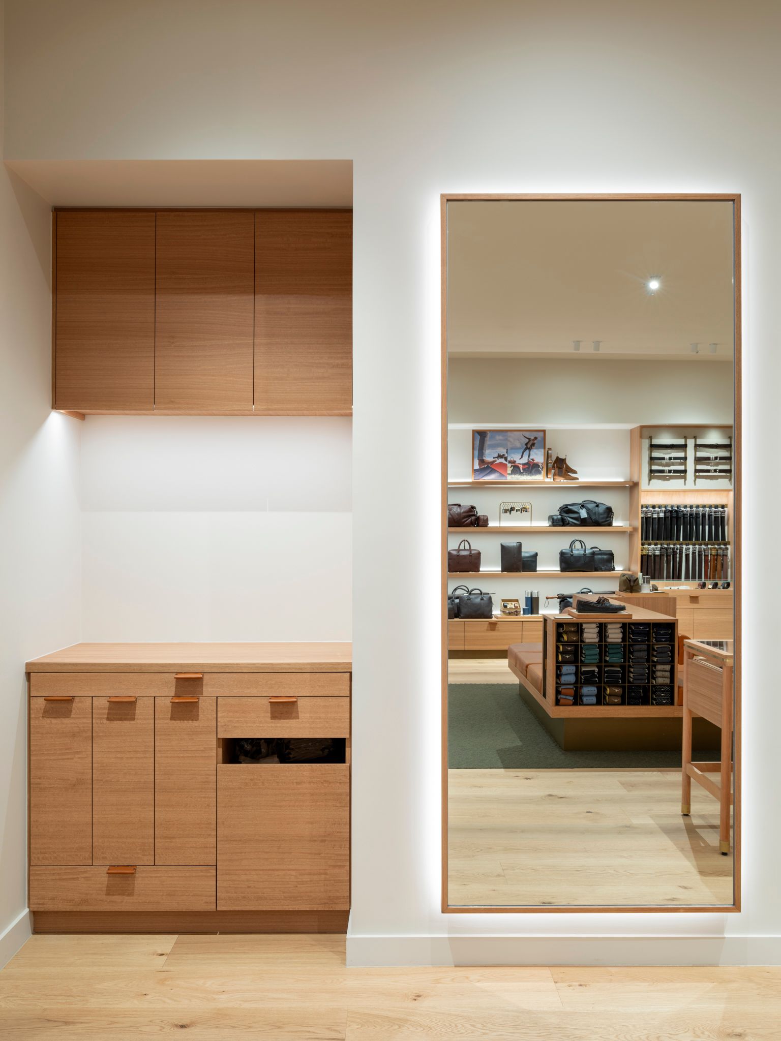 Interior of a store with a large mirror. Wooden cabinetry and display shelves are visible in the reflection.