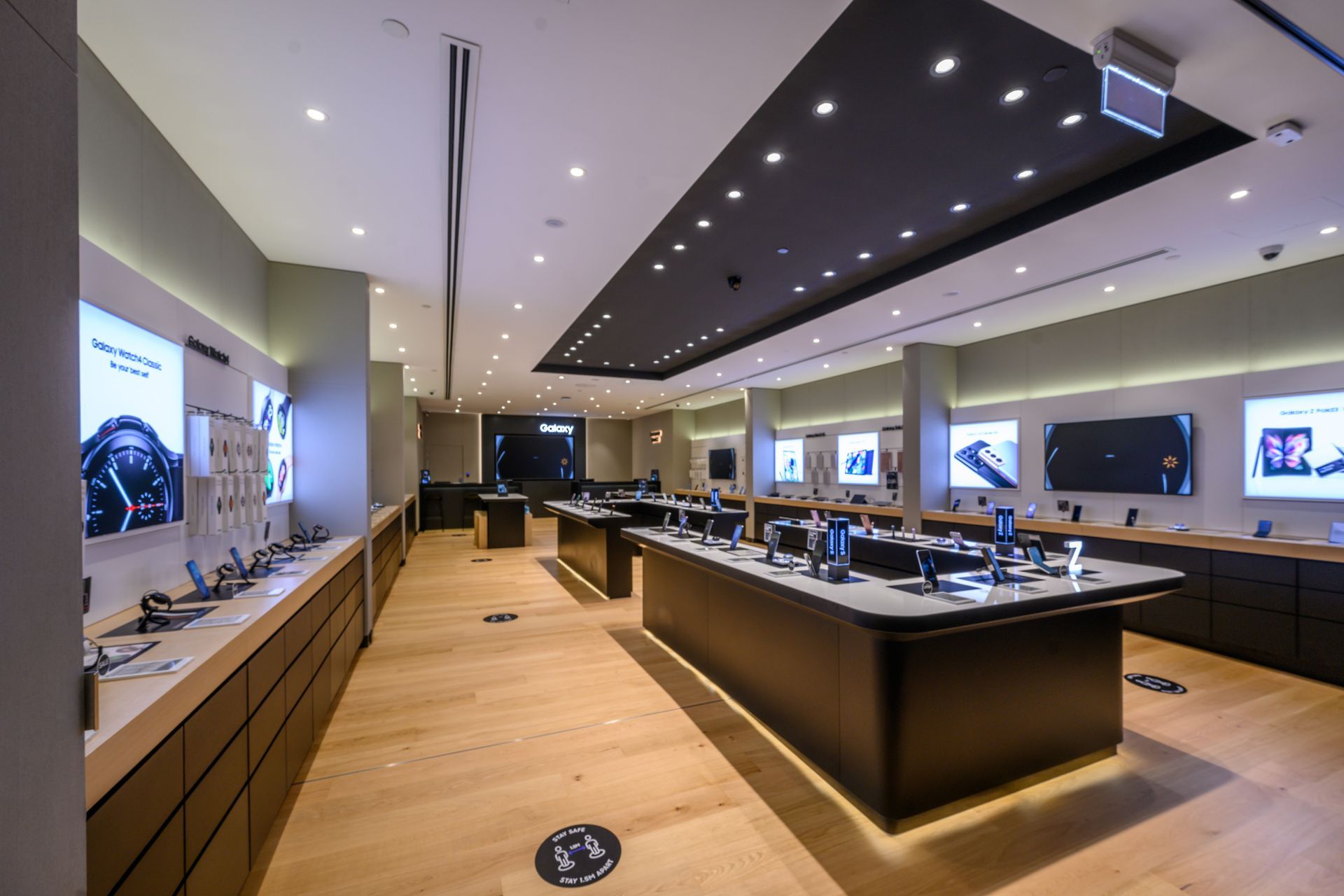 Inside of a modern tech store, products displayed on tables and lit wall displays.