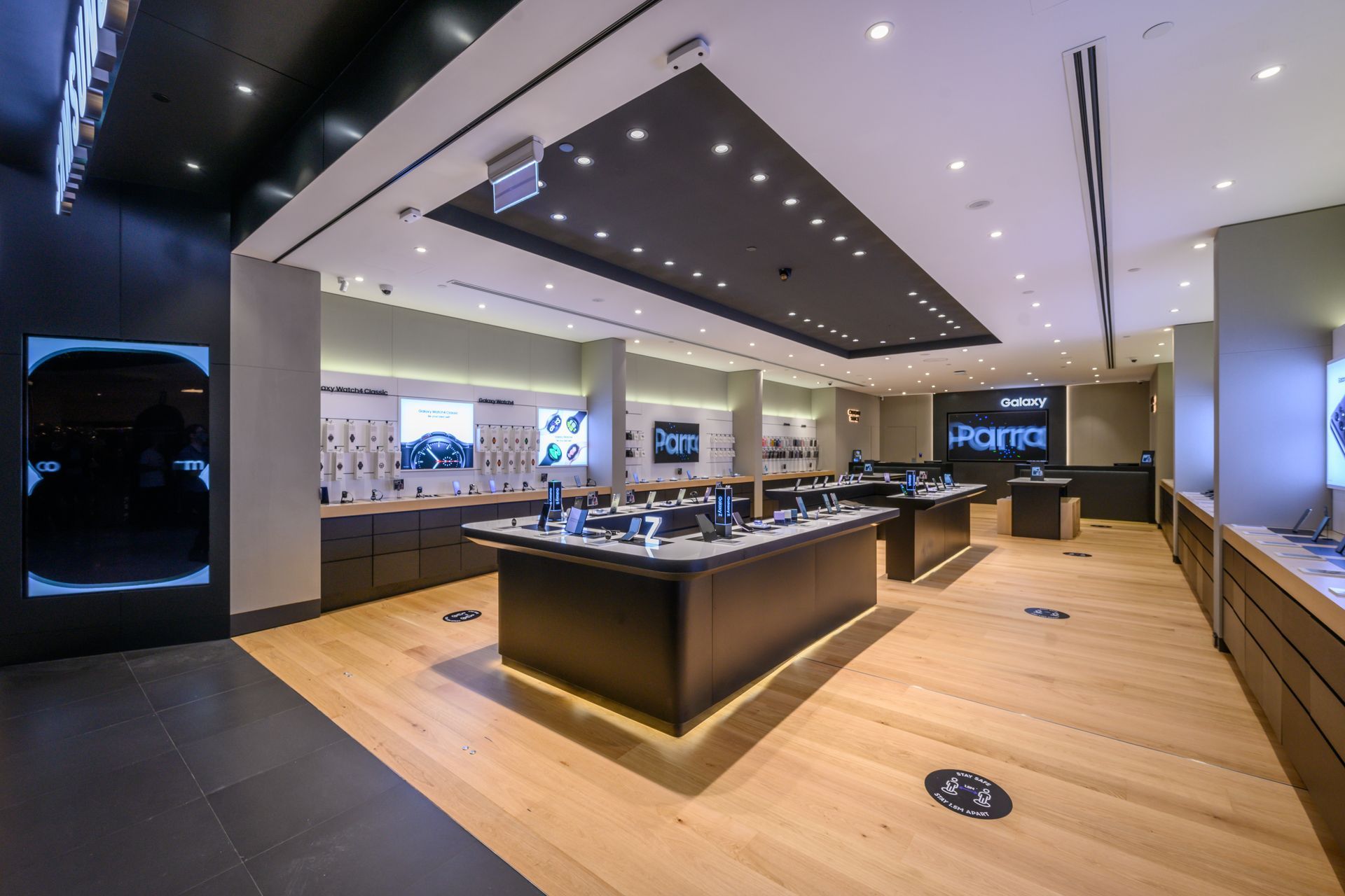 Modern electronics store interior with display tables, bright lighting, and wooden floors.