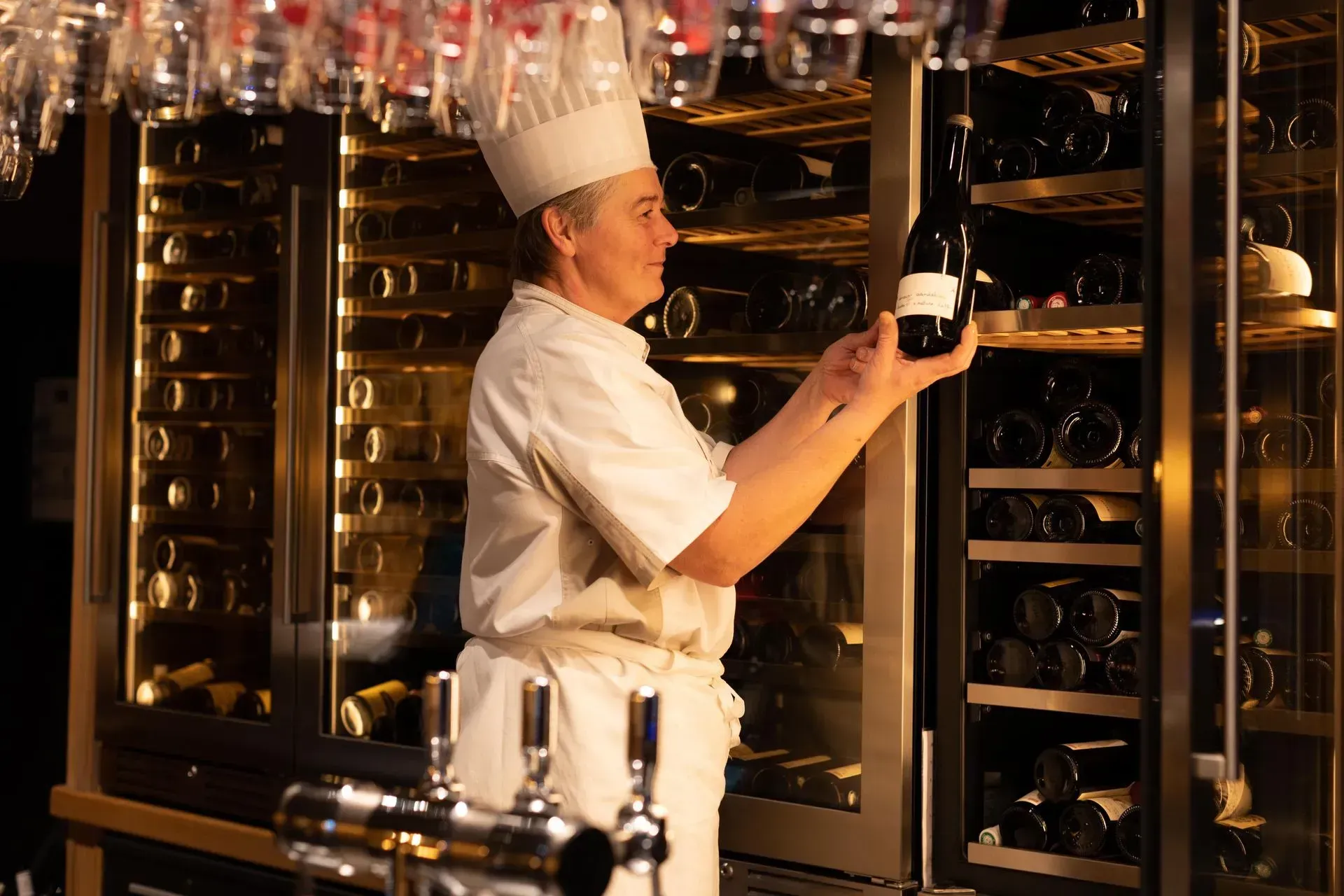 Un chef tient une bouteille de vin devant un refroidisseur à vin.