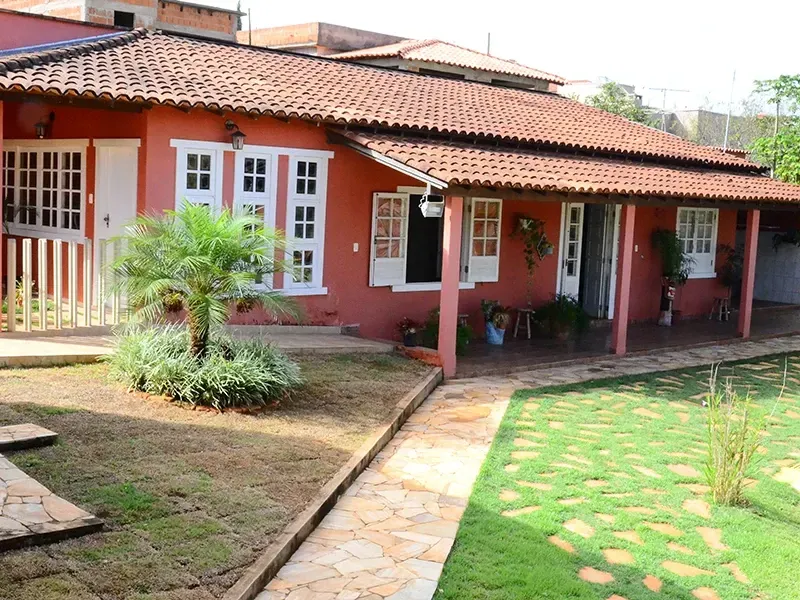 Casa vermelha com janelas de moldura branca, telhado de telha vermelha e caminho de pedra que atravessa um quintal verde.