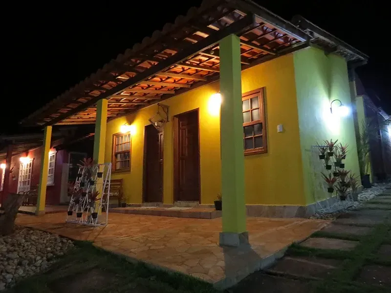 Prédio amarelo à noite com varanda iluminada, portas e janelas de madeira e telhado de telhas.