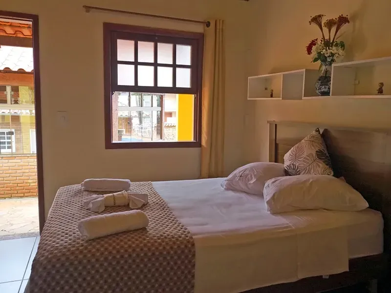 Quarto com cama, janela, porta aberta e prateleiras decorativas.