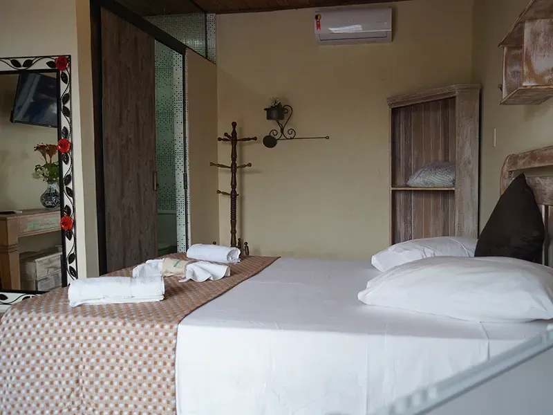 Quarto com cama, toalhas, espelho, cabideiro e pequena prateleira.