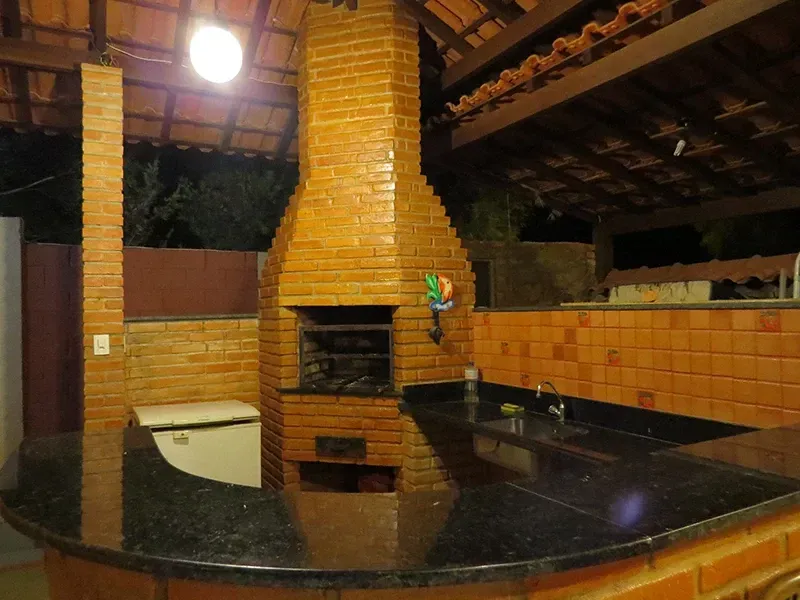 Churrasqueira de tijolos com bancada preta, sob um telhado de telhas.