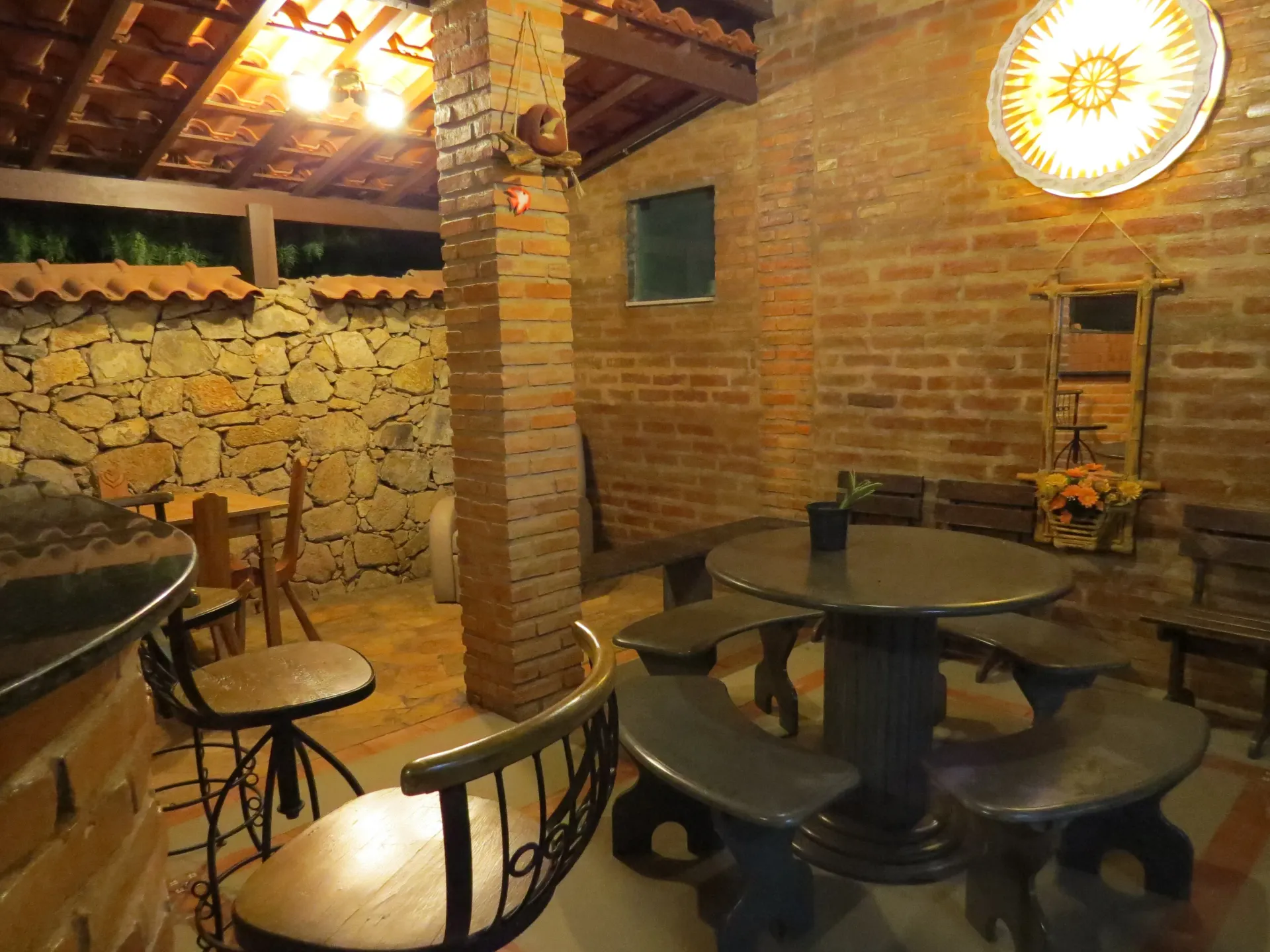 Aconchegante pátio externo com paredes de tijolo e pedra, móveis de madeira e iluminação acolhedora.