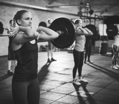 A woman is lifting a barbell over her head in a gym.