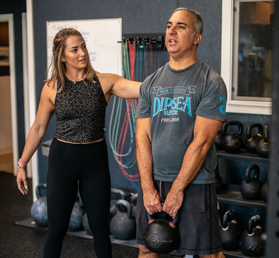 A man and a woman are standing in a gym holding kettlebells.