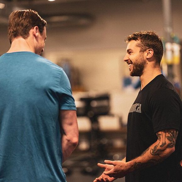 A man with a tattoo on his arm is talking to another man