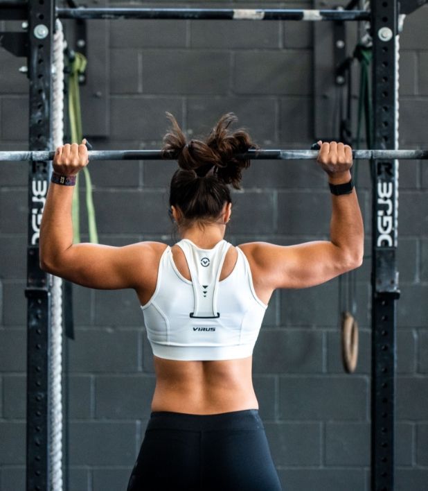 A woman is doing a pull up on a bar in a gym.