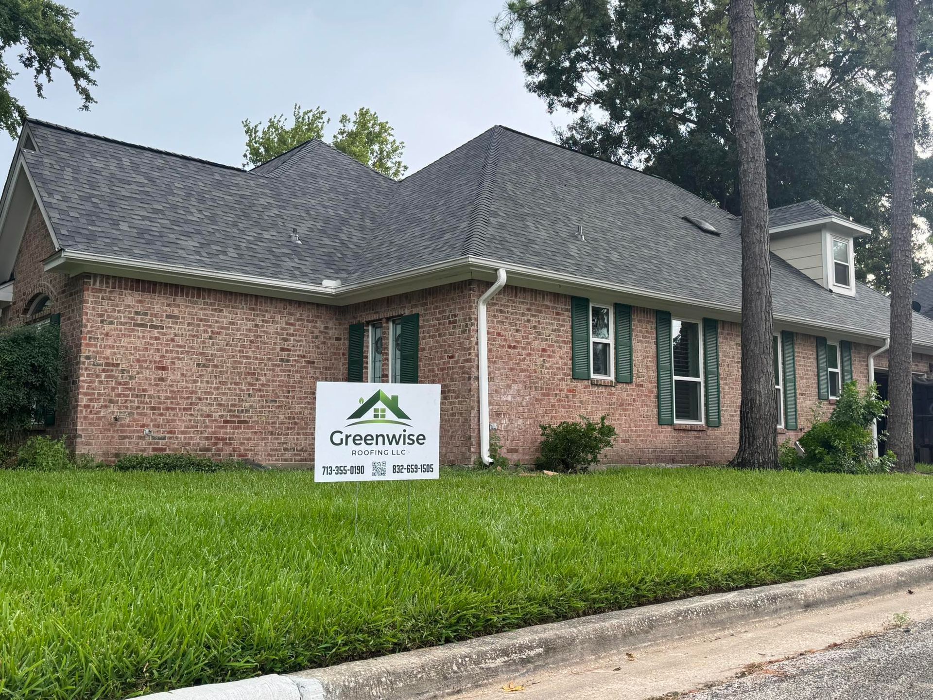 A brick house with a roof that has been installed and a sign in front of it.
