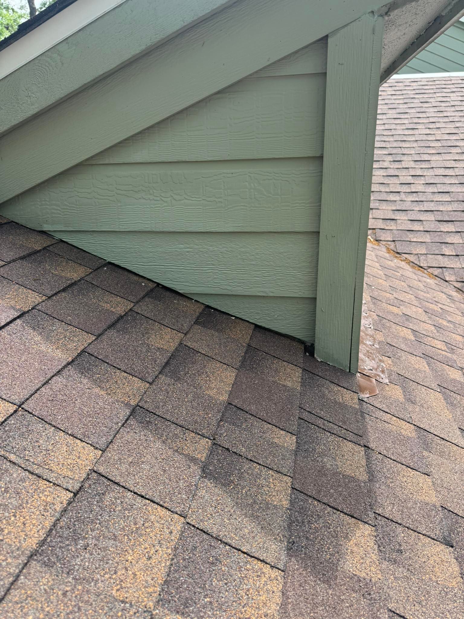 A close up of a roof with a green siding and a brown shingle roof.