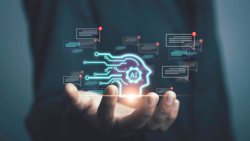 Hand holding a glowing AI circuit board head, surrounded by speech bubbles, symbolizing artificial intelligence.
