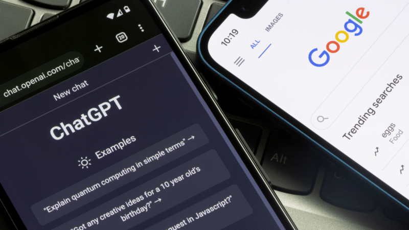Two smartphones, one displaying ChatGPT interface, the other Google search, on a laptop keyboard.