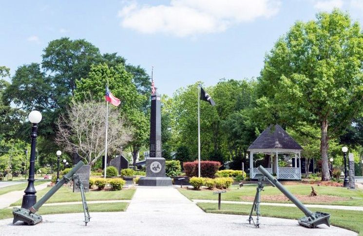 War memorial in a park setting with flags, a gazebo, and two cannons.