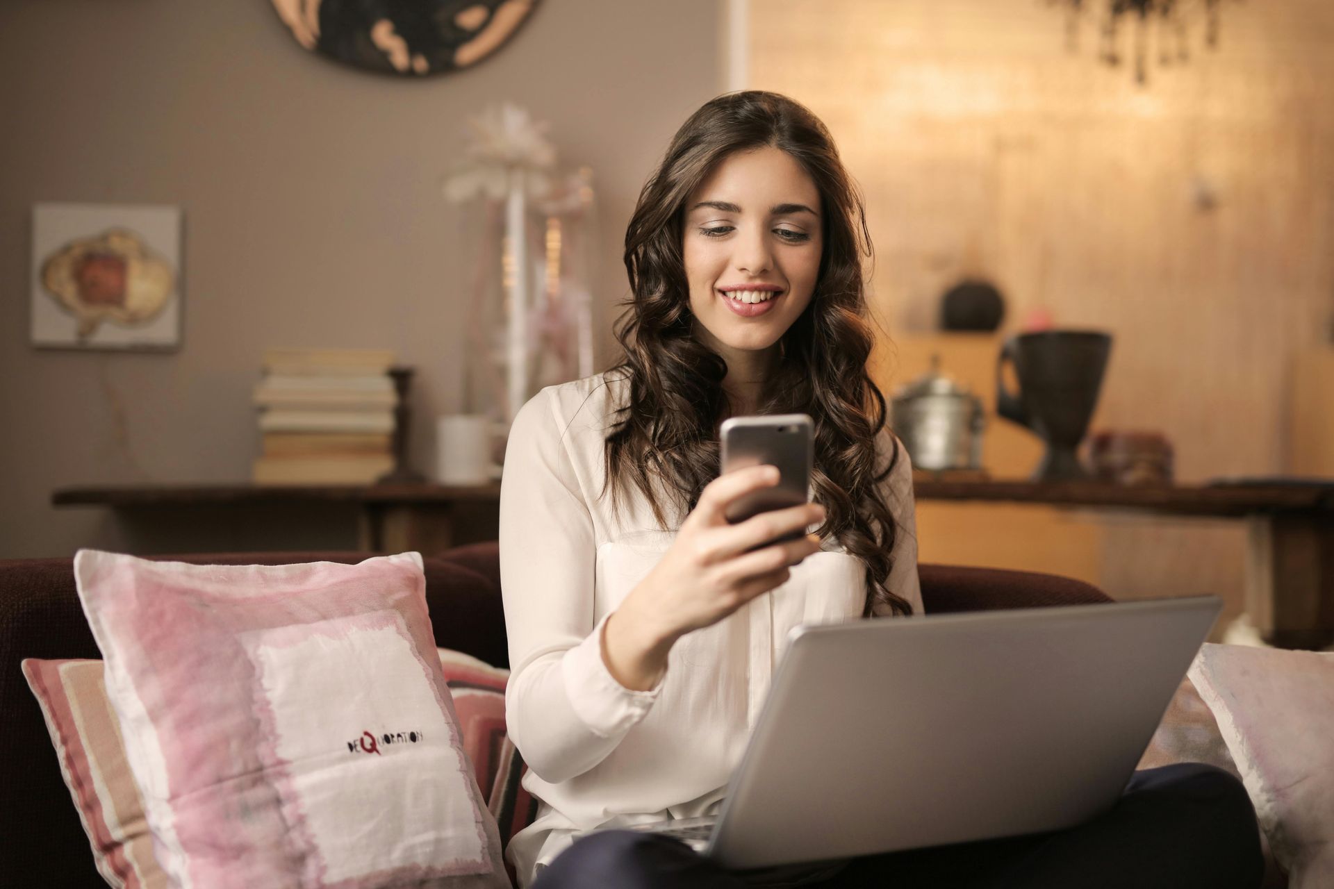 Woman with tattoos looking at her phone, surrounded by social media icons, in a cafe with brick wall.