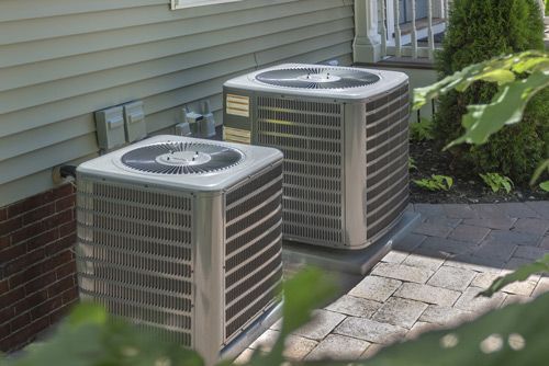 Two air conditioners are sitting on the side of a house.
