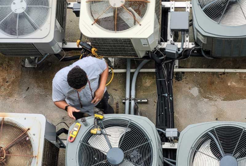 A man is working on an air conditioner on top of a building.