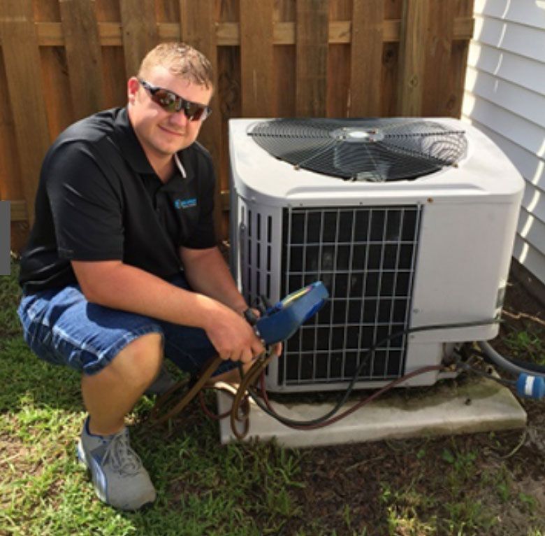 A man wearing sunglasses is kneeling next to an air conditioner