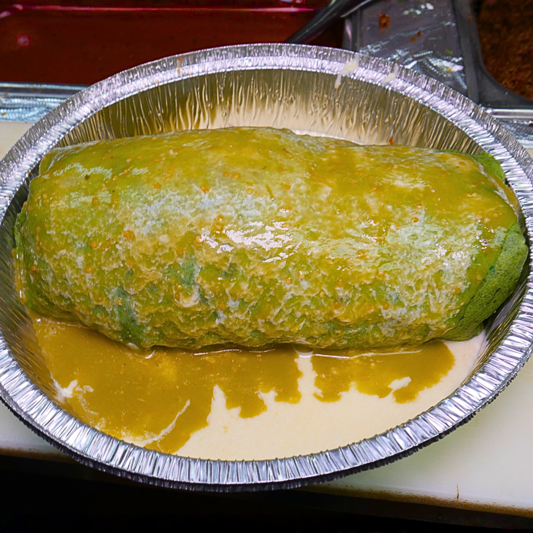 A large burrito covered in green sauce, in a foil container.