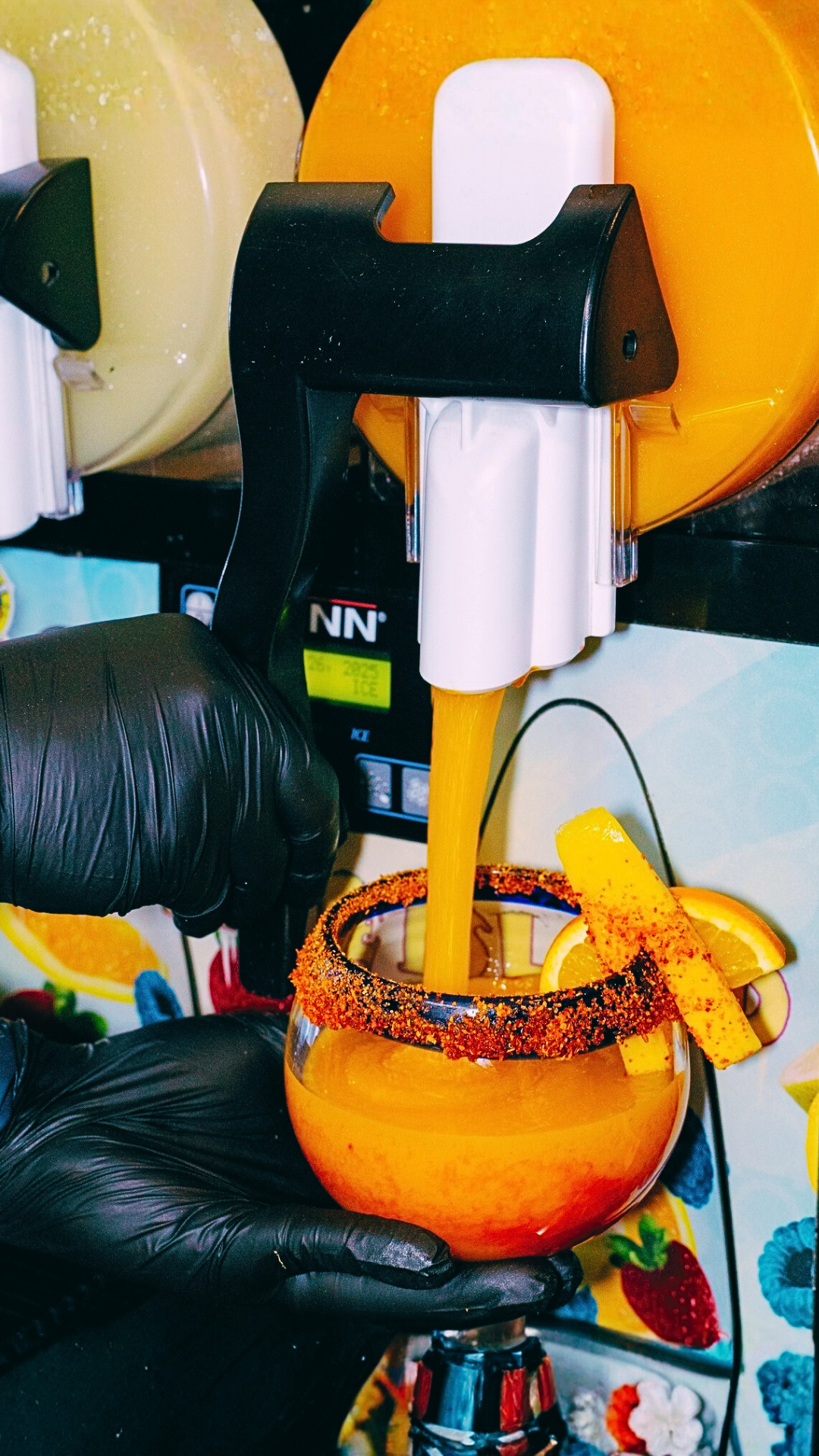 Margarita being poured into a glass rimmed with chili powder, garnished with an orange slice.