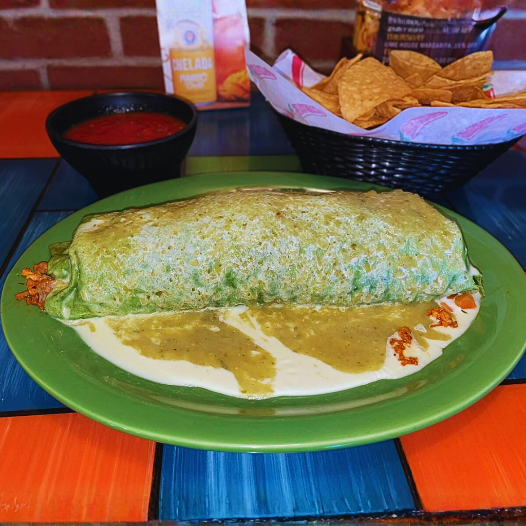 Burrito on a green plate, covered in sauce, with chips and salsa.