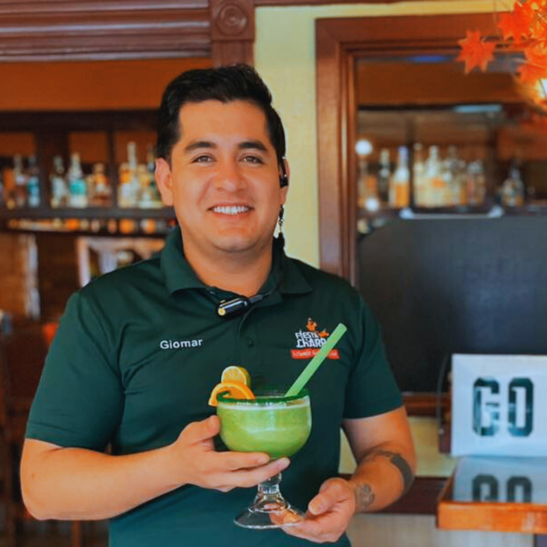 Smiling Fiesta Charra East Lansing bartender proudly holding a large, colorful margarita at the restaurant’s bar counter.