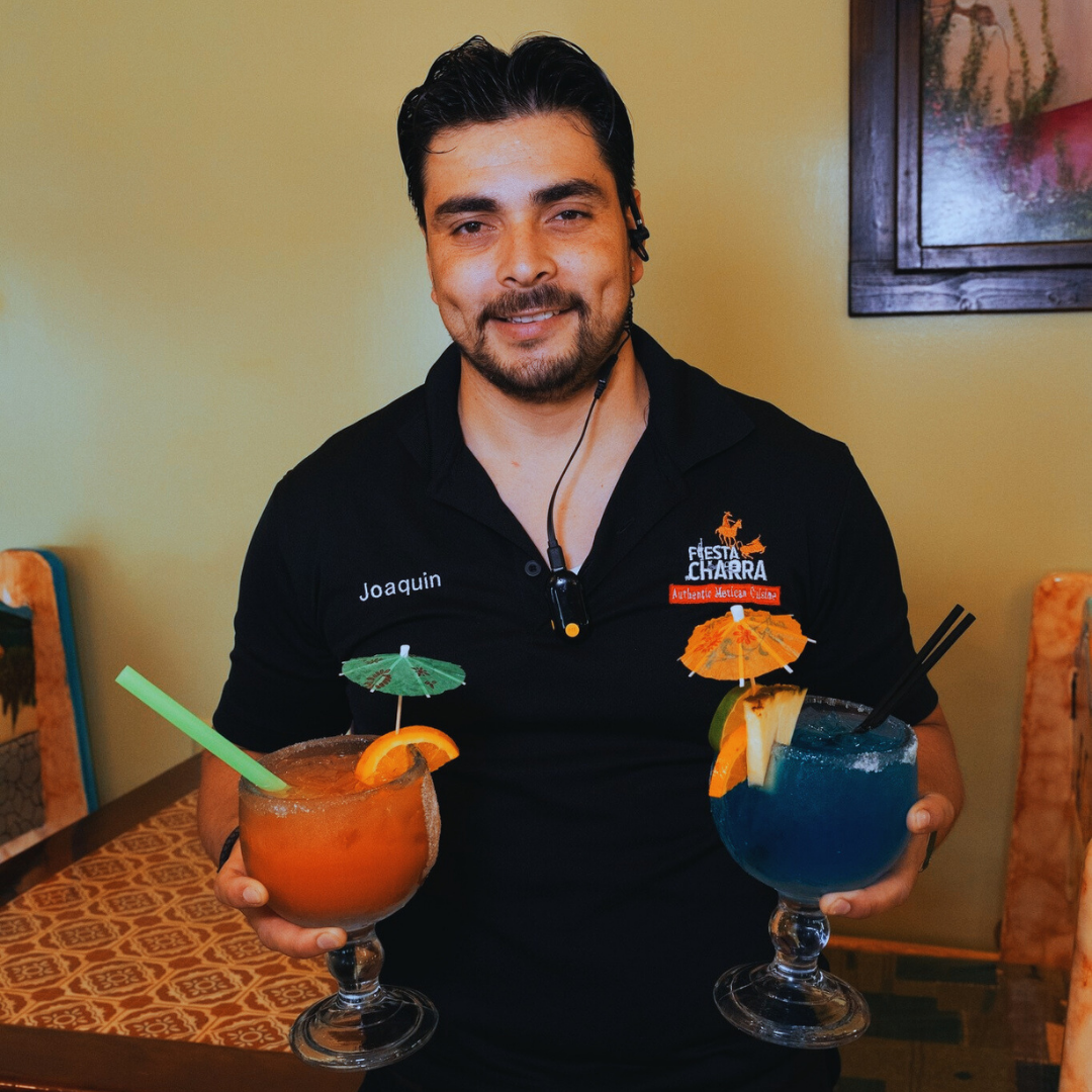 Fiesta Charra East Lansing bartender presenting two vibrant, garnished margaritas, ready to serve guests at their table.