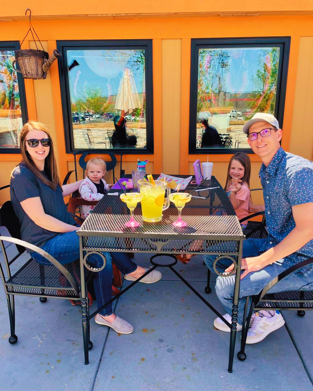 Family of four at outdoor restaurant table with drinks.