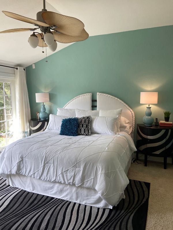 Bedroom with white bed, teal wall, zebra-striped nightstands, and a fan.