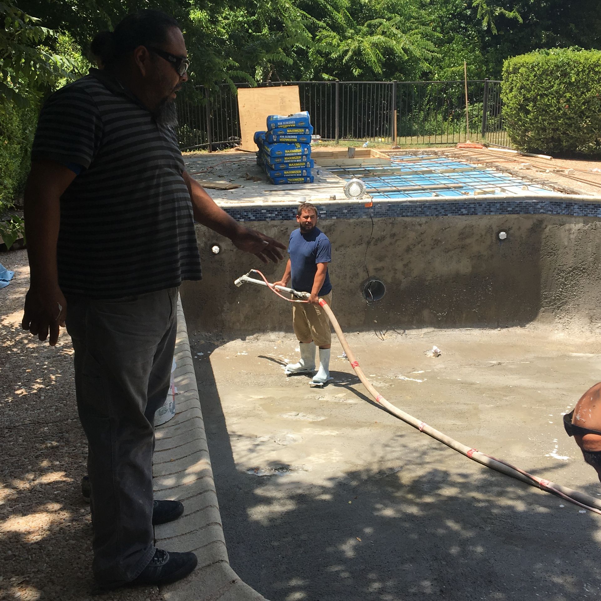 Men working on a pool renovation. One points, the other holds a hose, setting is outdoors.