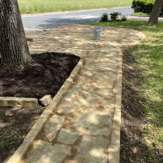 Stone pathway and circular patio with a tree, surrounded by grass and mulch.