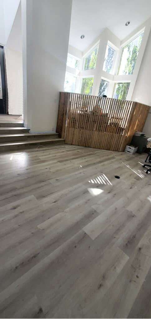 An open-concept room with light wood-look flooring, tall white walls, and a wooden trellis partition.