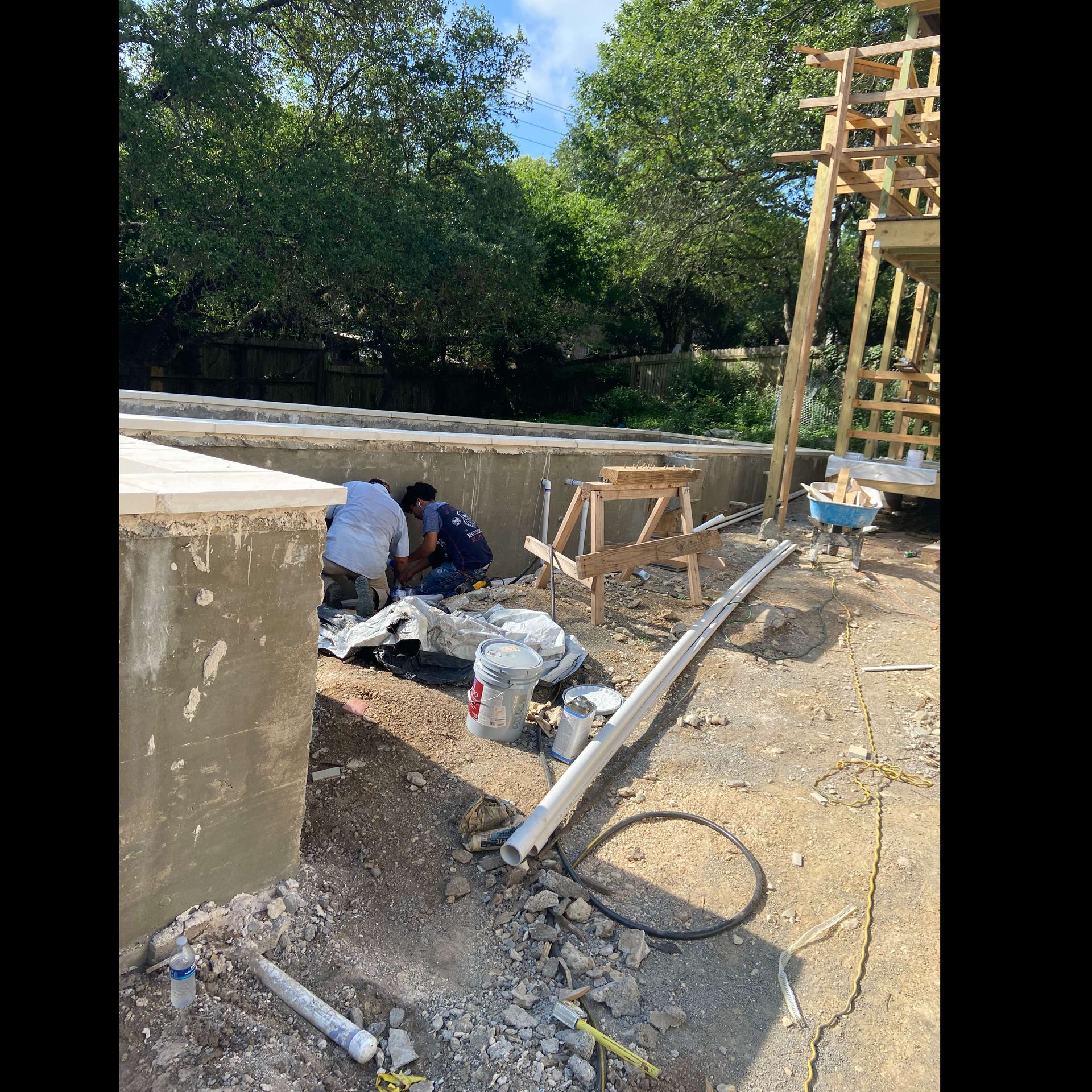 Construction site with workers near concrete walls, building wooden structures. Outdoors, sunny.