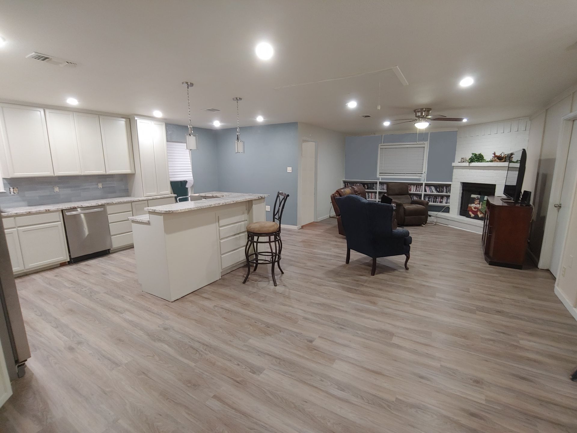 Open-concept kitchen and living room with white cabinets, blue wall, and wood-look flooring.