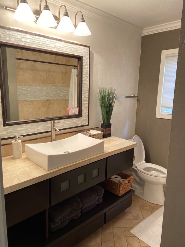 Bathroom with dark cabinets, white sink, toilet, mirror, and brown wall accents.