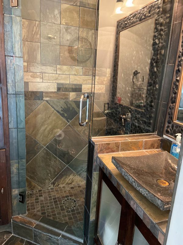 Bathroom with a stone-tiled shower, dark wooden vanity, and a unique stone sink.