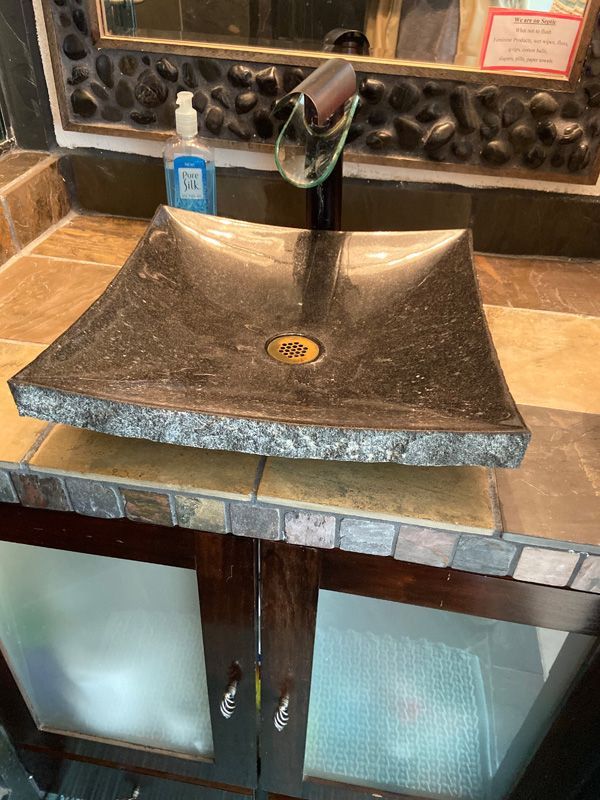 Black square stone sink on a tiled countertop, with a dark faucet and cabinet below.
