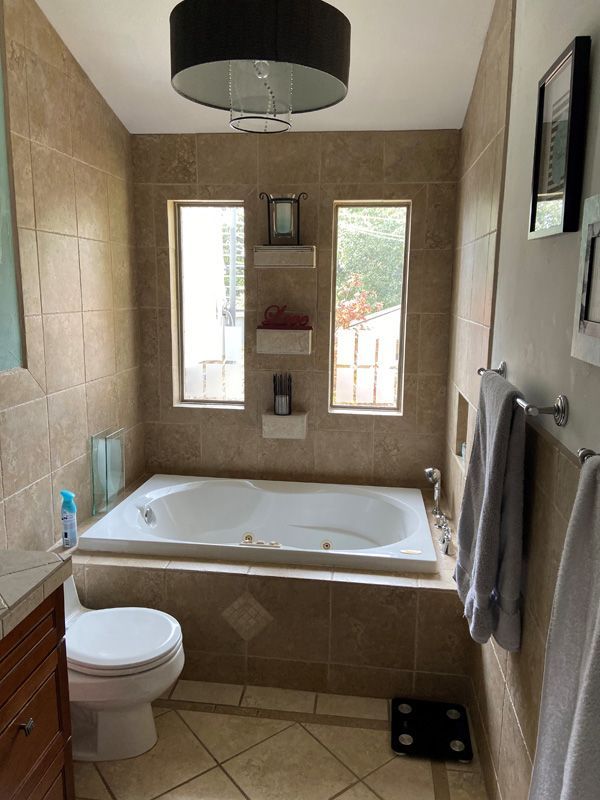 Bathroom with a built-in jacuzzi tub, two windows, and tan tile walls. A black light fixture hangs above.