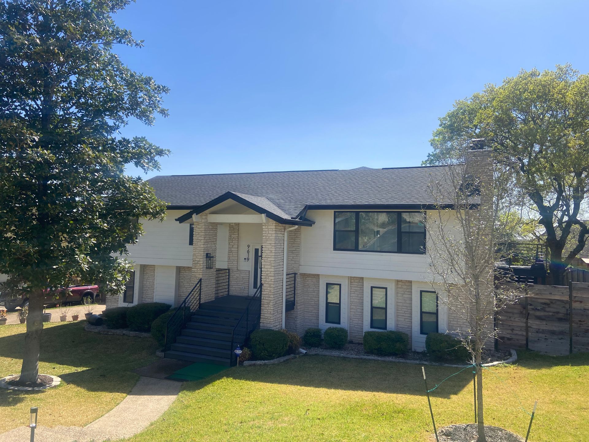 Two-story white house with dark roof and stone accents, sunny day.