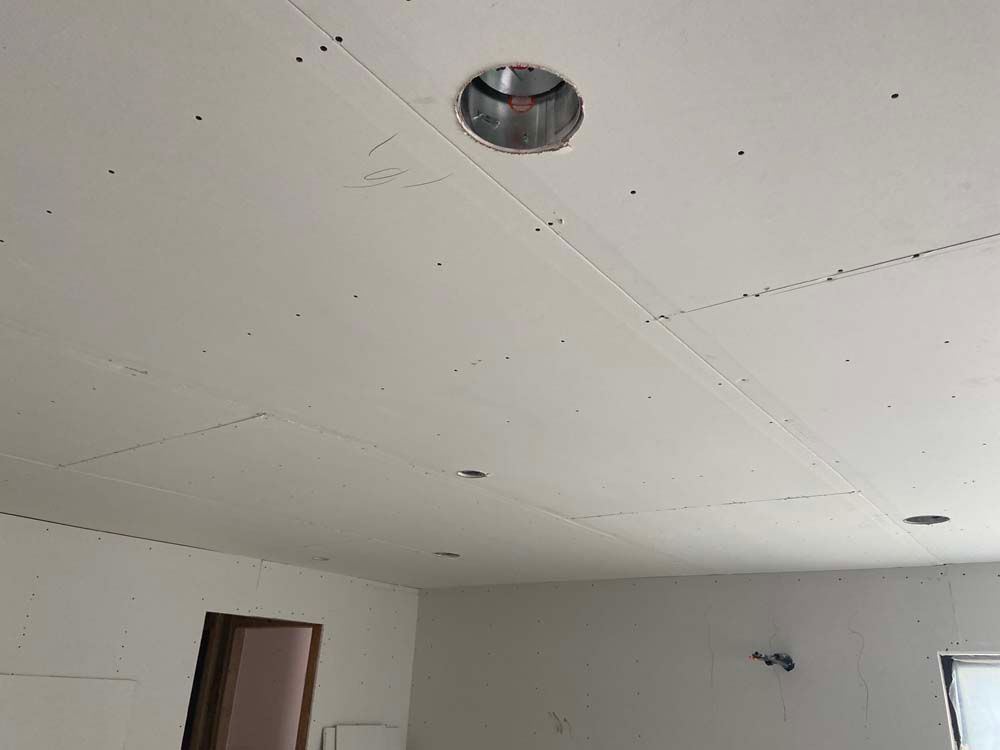 Drywall ceiling with recessed lighting and seams, in a room under construction.